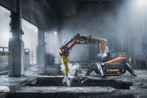 Bilningsrobot med hydraulhammare river betong i en dammig byggnad