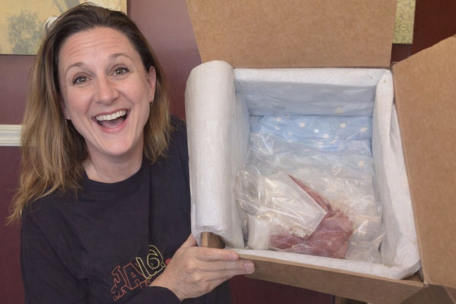 En glad kvinna som packar upp en matkasse med isolering och ingredienser.