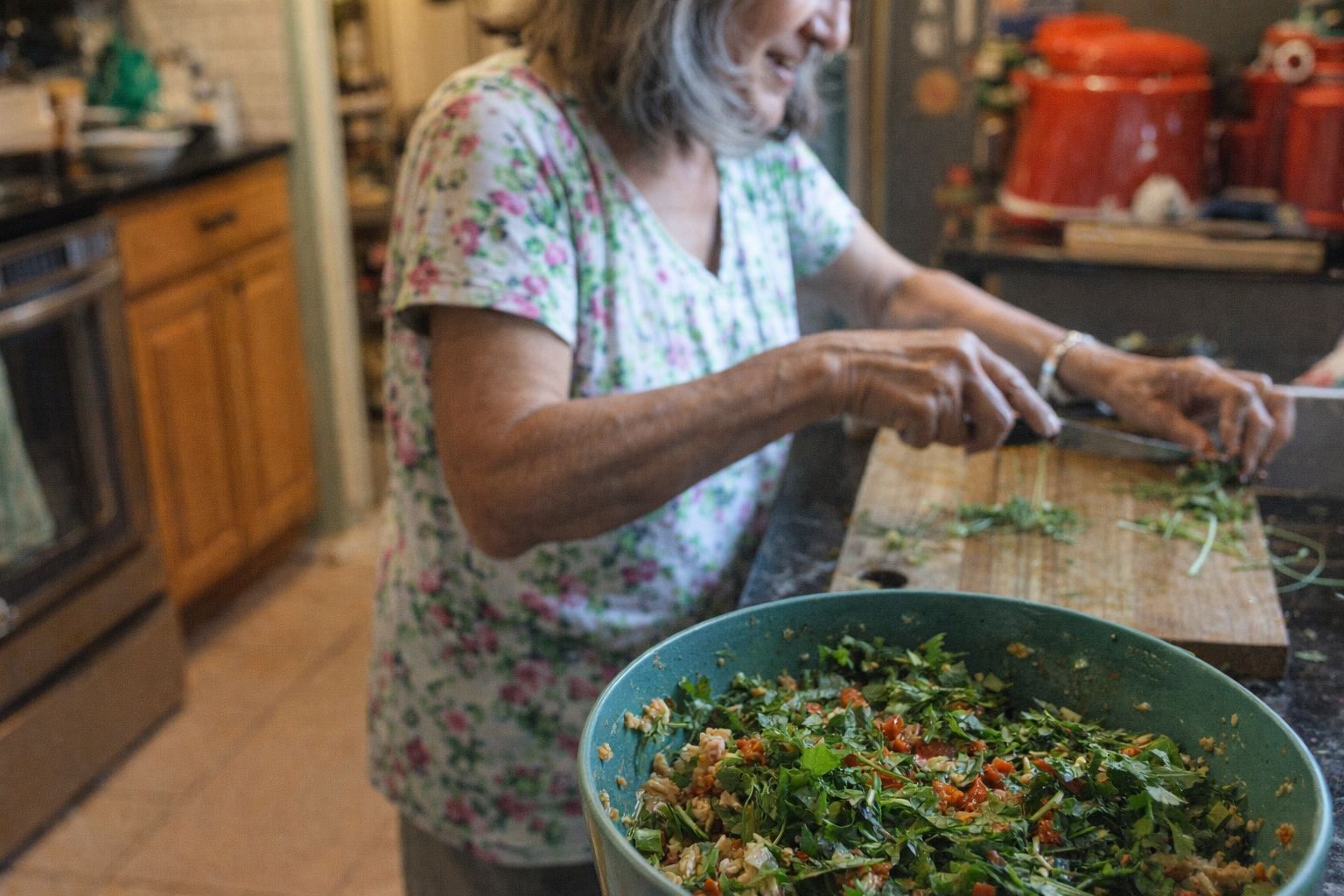 En äldre kvinna lagar en hälsosam middag med färska örter och grönsaker i ett kök.